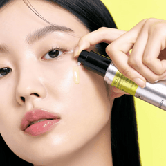 Person applying a cosmetic product to their face with a yellow background