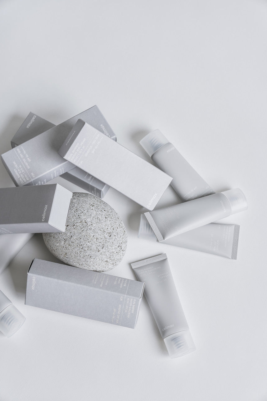 Collection of skincare products including boxes, tubes, and a round product on a light gray background