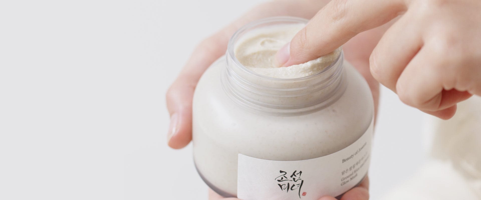 Hand holding a jar of cream with a visible label on a light background