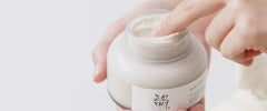 Hand holding a jar of cream with a visible label on a light background