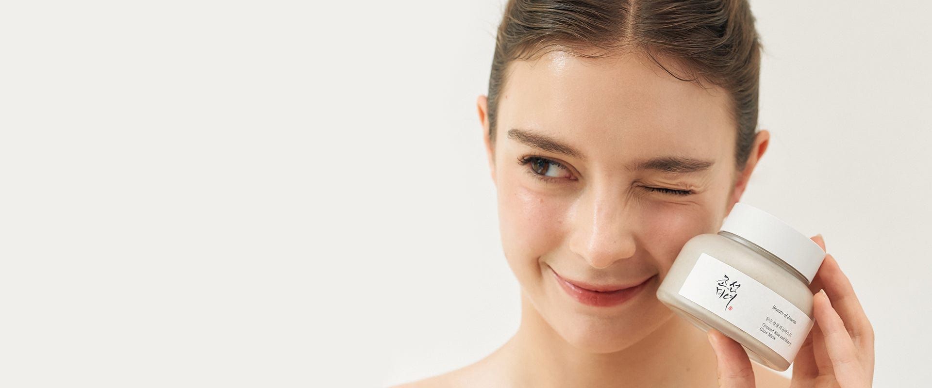 Woman holding a skincare product with a plain background