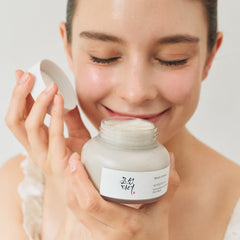 Woman holding a jar of cream with a visible brand label on a plain background
