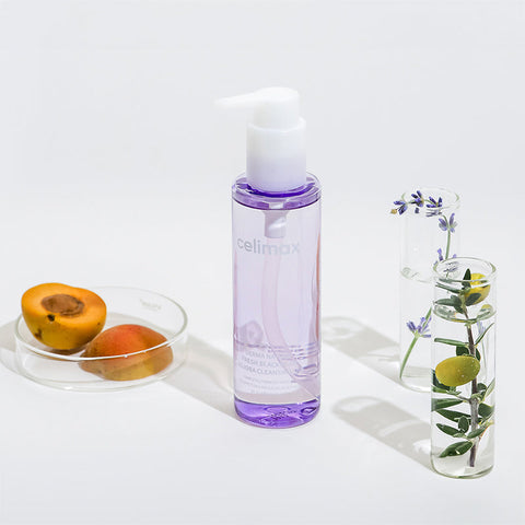 Clear bottle with purple cap labeled 'celimax' on a white surface with fruits and a glass container with flowers.