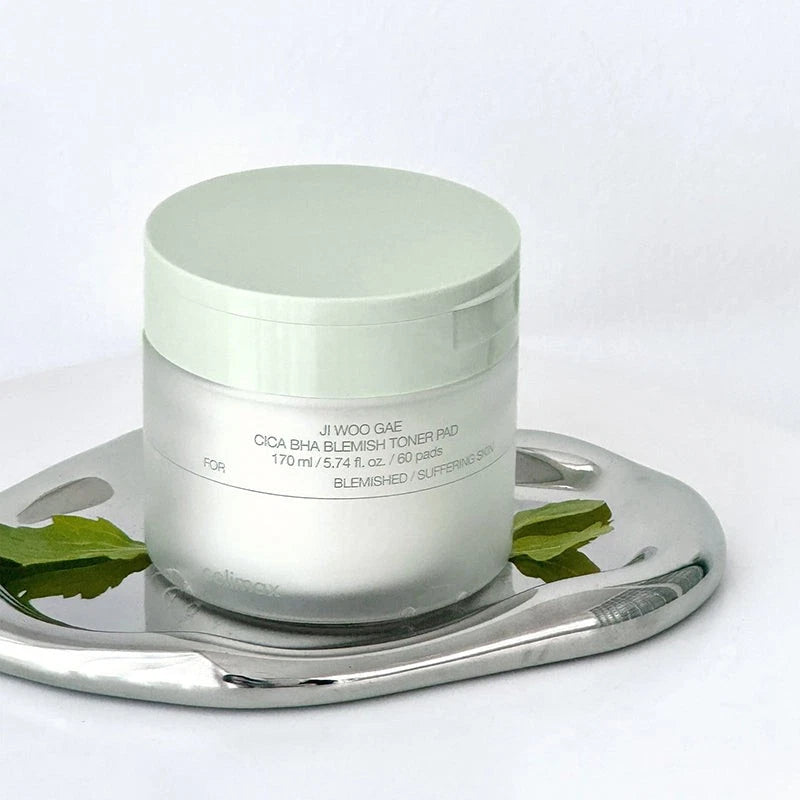 Skincare product jar on a metallic tray with green leaves on a white background