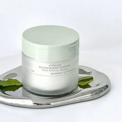 Skincare product jar on a metallic tray with green leaves on a white background